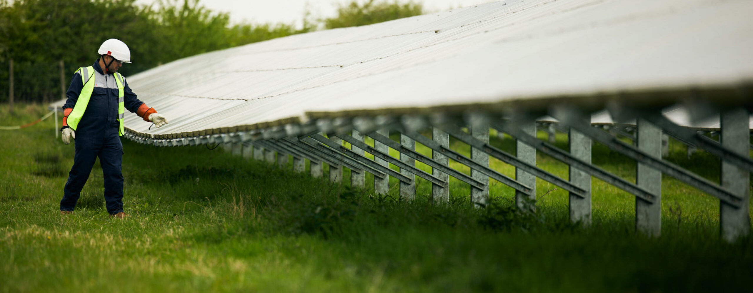 Worker in high-vis gear inspecting solar panels on a solar farm