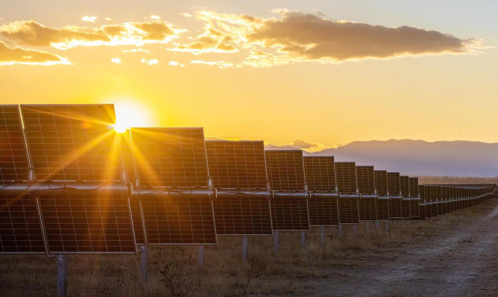 Sunset at a solar farm, sun shining through the panels