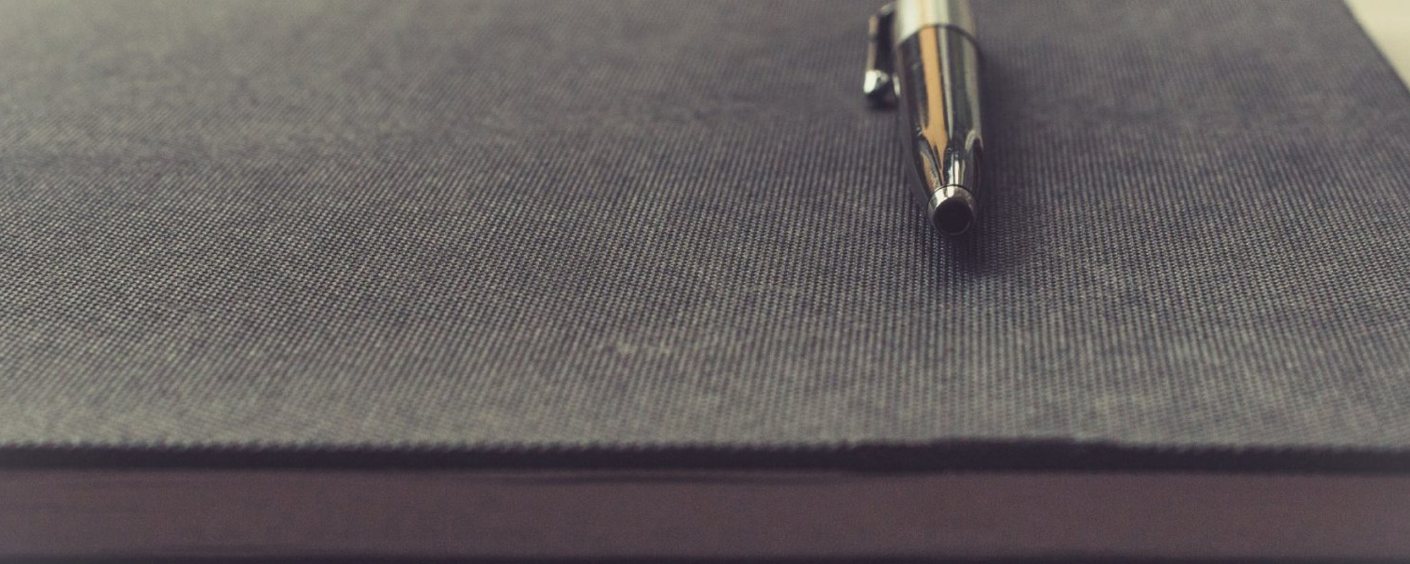 Close-up of a silver pen resting on a gray notebook, ready for writing or note-taking.