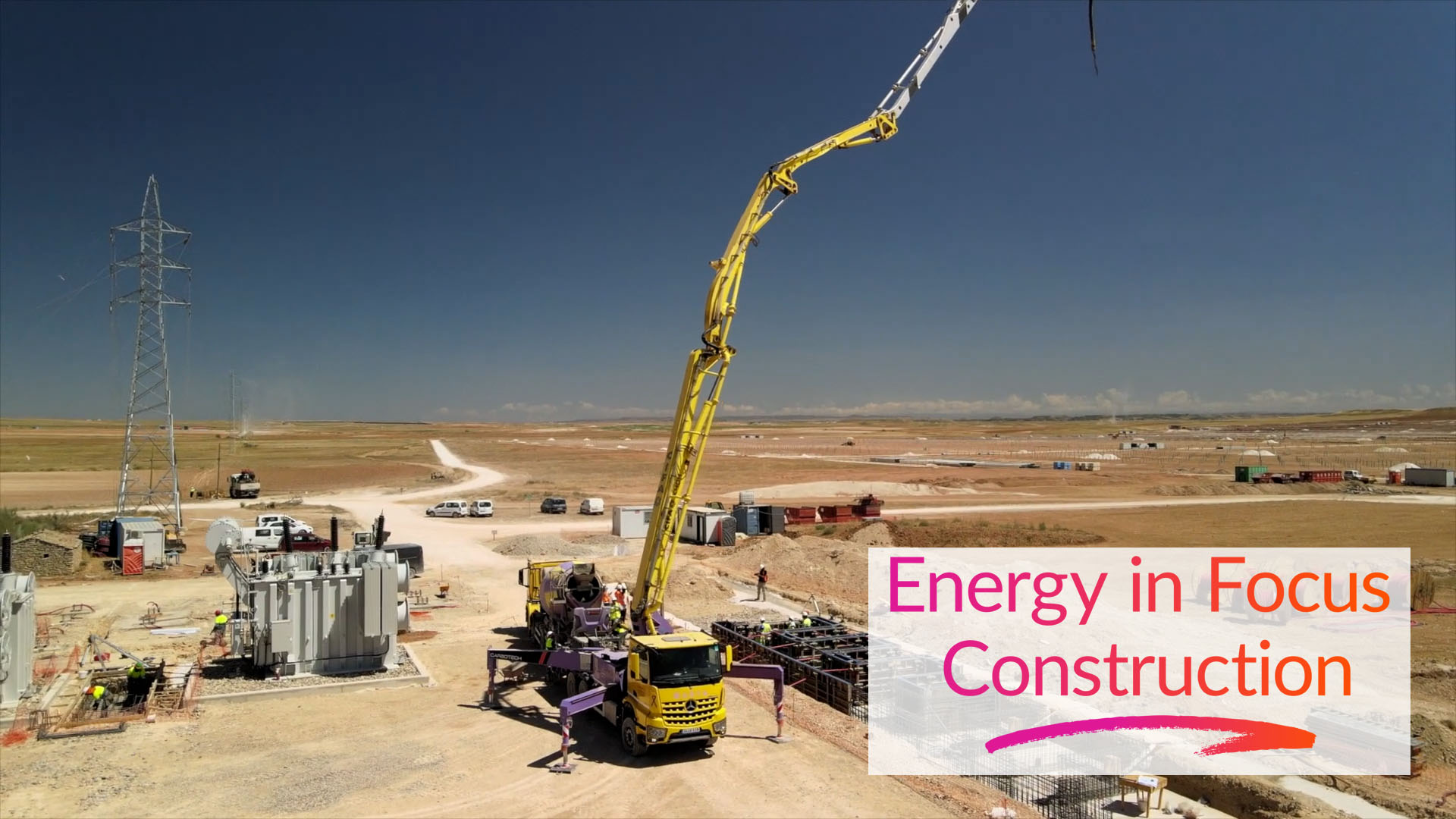 A construction site of a solar project in a wide, open landscape with a yellow concrete truck in operation. Several workers are present and electrical infrastructure is visible nearby. The image includes the text ‘Energy in Focus Construction’ in pink and orange on a white overlay.